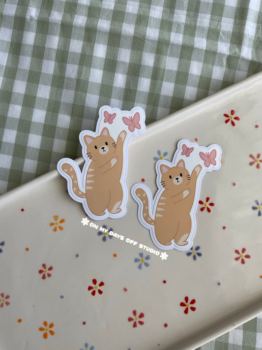 Cute vinyl sticker of a orange cat playing with butterfly stamp