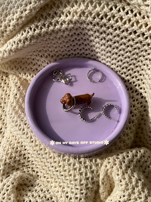 Small brown dachshund figurine on a purple jewelry dish or trinket dish