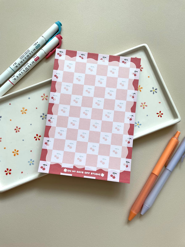 Red and pink checkered notepad with cute little cherries in the pink boxes of the print