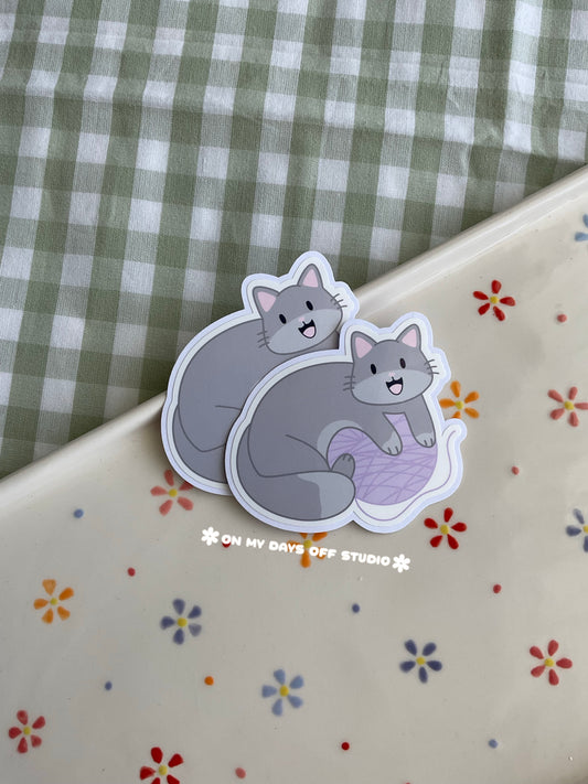 Cute vinyl sticker of a cute grey cat playing with yarn
