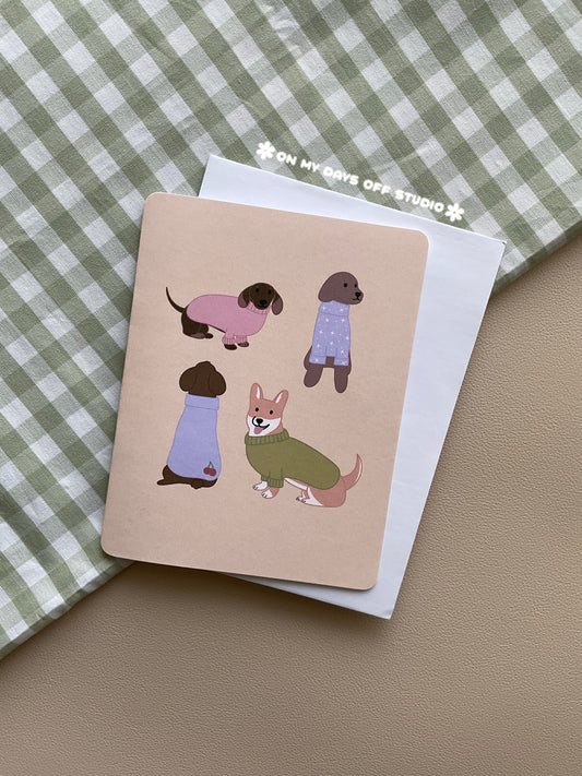 Soft yellow greeting card with 4 illustrations of dog in sweaters. A dachshund, labrador, corgi and poodle.