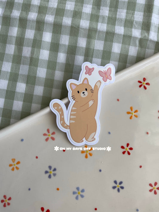Cute vinyl sticker of a orange cat playing with butterfly stamp