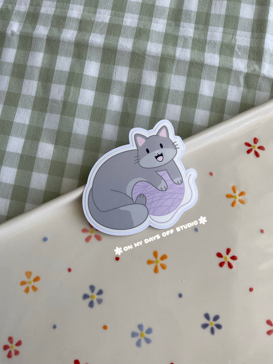 Cute vinyl sticker of a cute grey cat playing with yarn