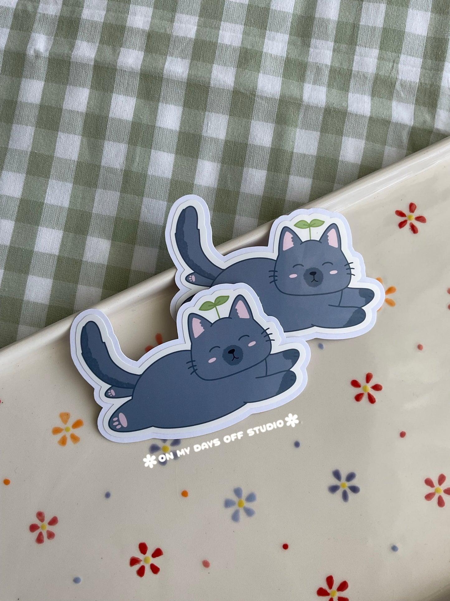 Cute vinyl sticker of a cute grey cat with a sprout on it's head and fully laying on it's belly