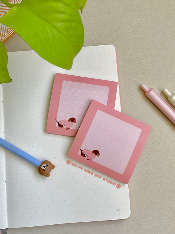 Cute pink sticky notes with a grid background and an adorable dachshund wearing a pink sweater in the bottom left corner