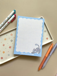 Grid notepad with a cute grey cat stretching in the bottom right corner. This notepad also has a blue wavy boarder. 