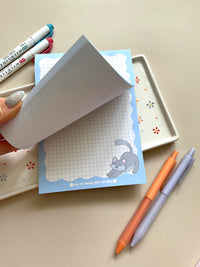 Grid notepad with a cute grey cat stretching in the bottom right corner. This notepad also has a blue wavy boarder. 