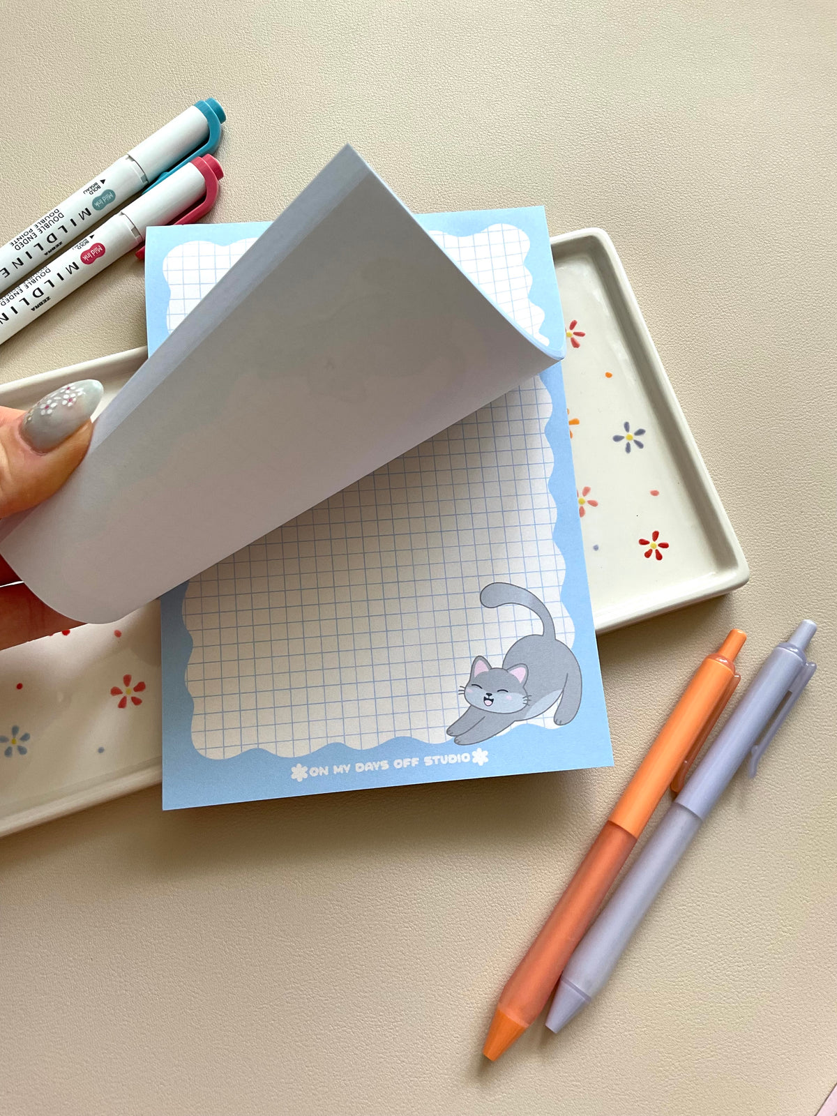 Grid notepad with a cute grey cat stretching in the bottom right corner. This notepad also has a blue wavy boarder. 