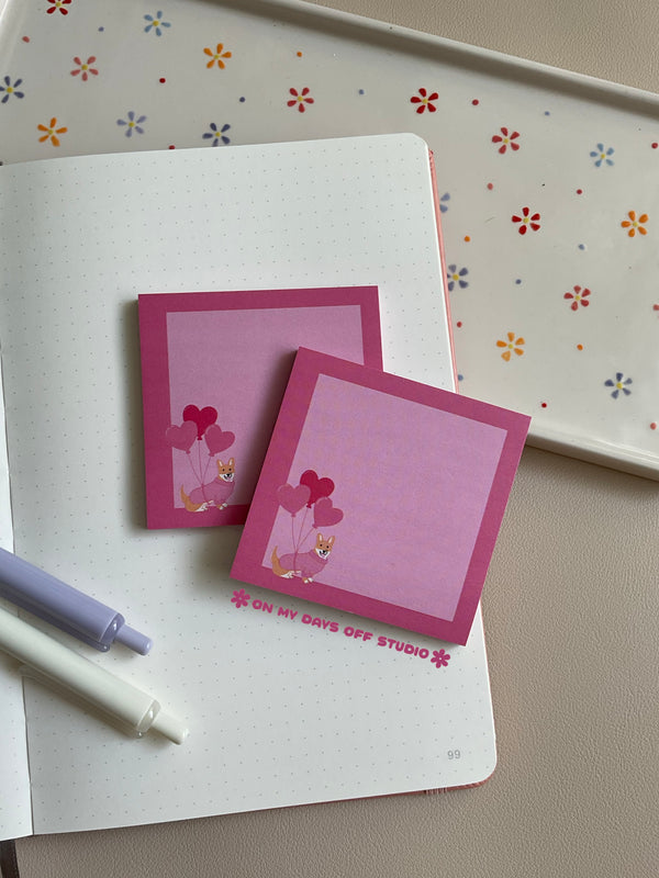 Pink sticky notes with a light pink background and darker pink boarder. There is a cute corgi wearing a sweater and carrying 3 heart balloons in the bottom left corner.