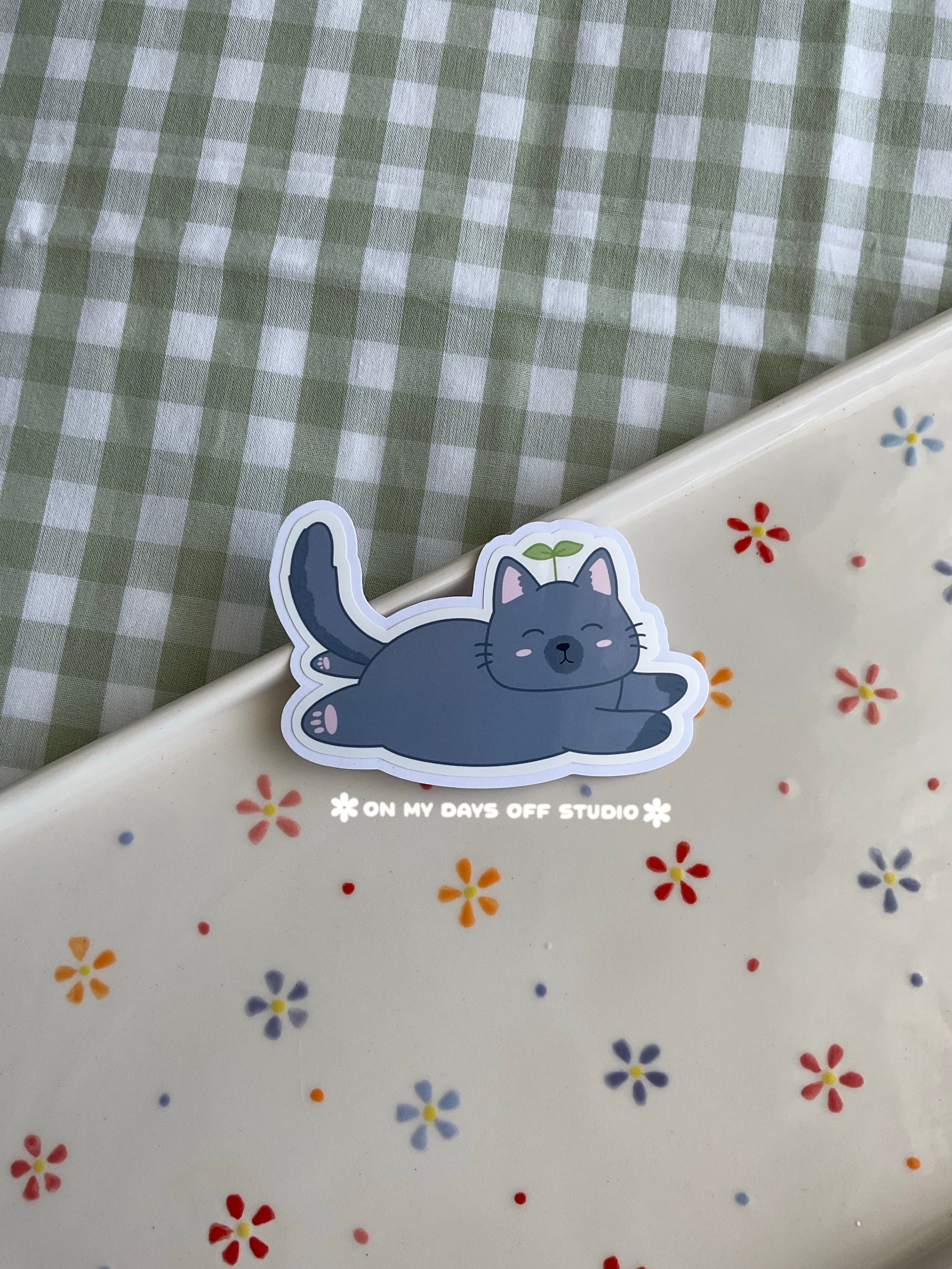 Cute vinyl sticker of a cute grey cat with a sprout on it's head and fully laying on it's belly