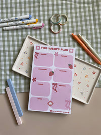 Weekly planner with a pink, red, bow and strawberry theme. It has sections for every day of the week and for notes.