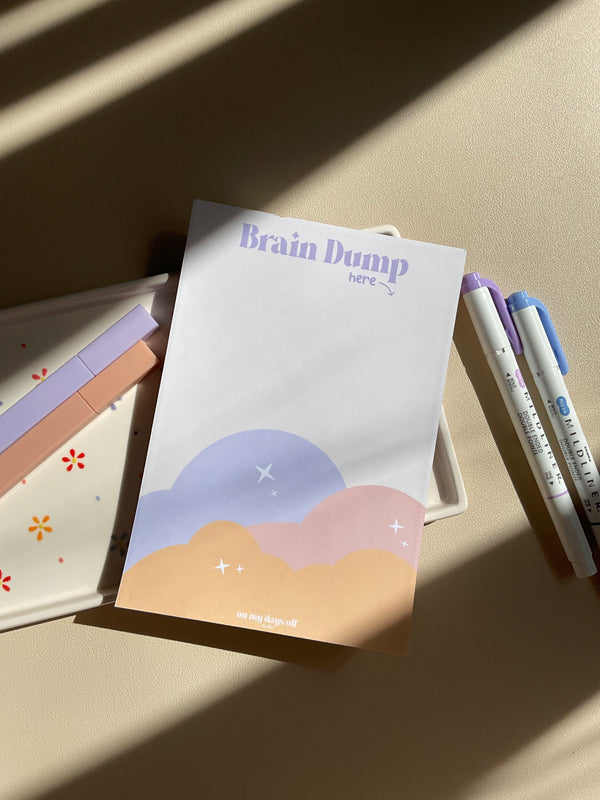 Cute beige notepad with a fun sunset cloud illustration at the bottom half. Brain Dump is noted in purple at the top. 