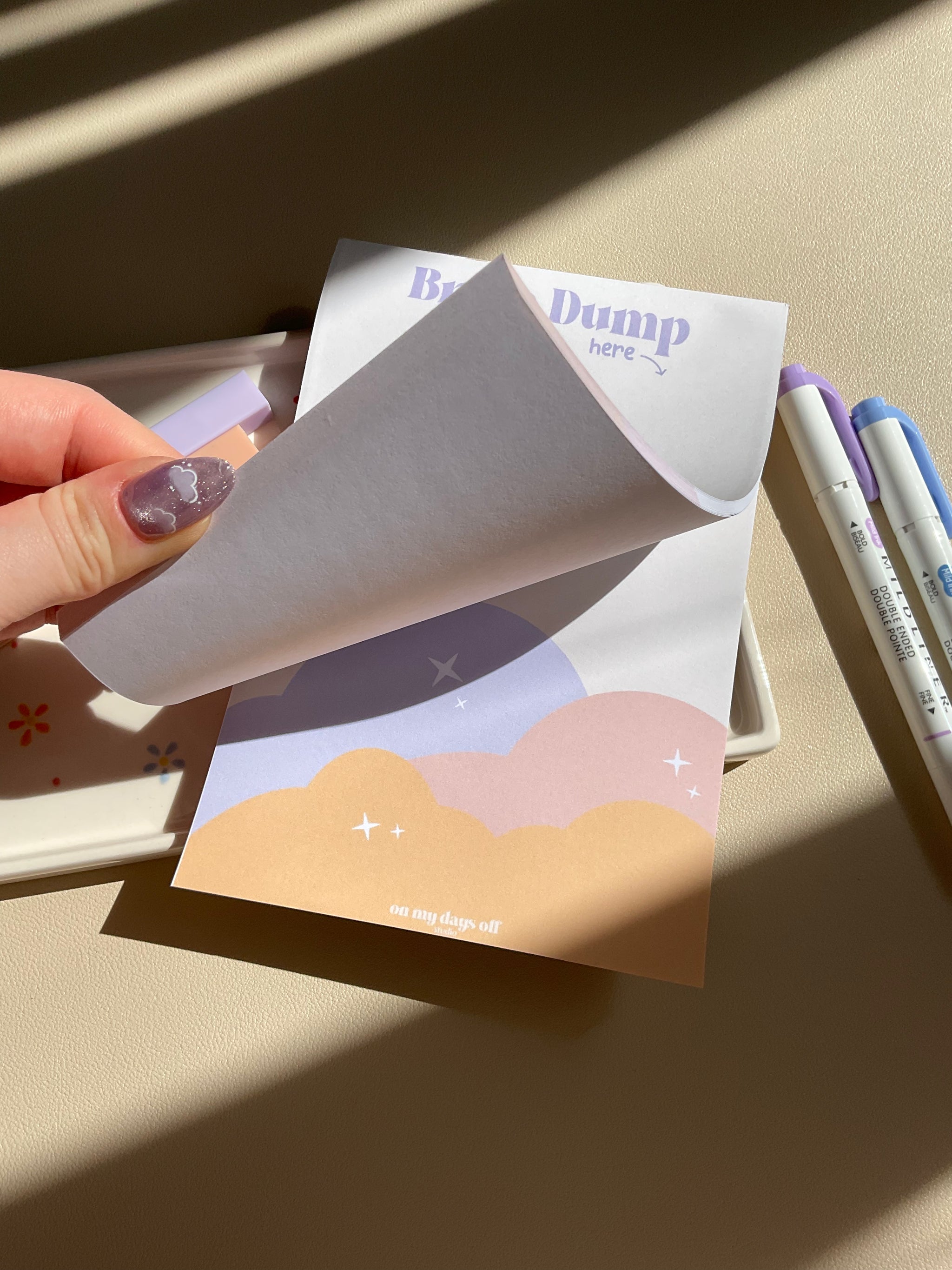 Cute beige notepad with a fun sunset cloud illustration at the bottom half. Brain Dump is noted in purple at the top. 