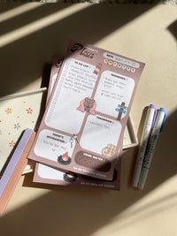 A daily planner notepad with a camp theme, featuring cute illustrations of a bear and camping related things. It has sections for a t do list, reminders, tomorrow list, today's affirmation and water in take tracker.