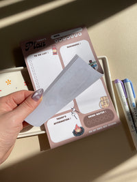 A daily planner notepad with a camp theme, featuring cute illustrations of a bear and camping related things. It has sections for a t do list, reminders, tomorrow list, today's affirmation and water in take tracker.