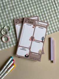 A daily planner notepad with a camp theme, featuring cute illustrations of a bear and camping related things. It has sections for a t do list, reminders, tomorrow list, today's affirmation and water in take tracker.