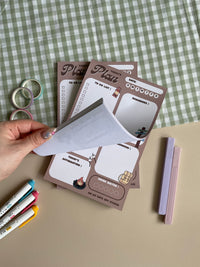 A daily planner notepad with a camp theme, featuring cute illustrations of a bear and camping related things. It has sections for a t do list, reminders, tomorrow list, today's affirmation and water in take tracker.