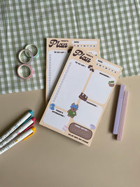 A daily planner notepad with a coffee theme. Features a place for your to do list. reminders, list for tomorrow, today's affirmation and a water intake tracker