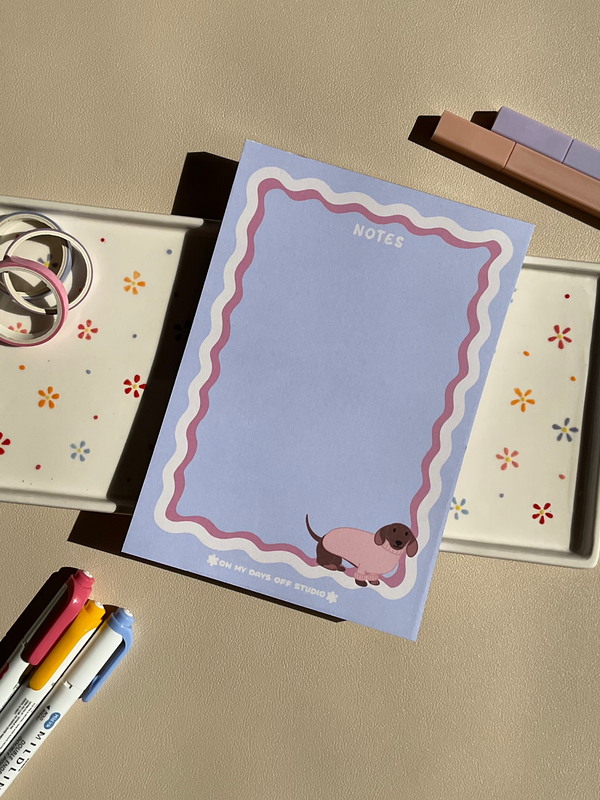 Cute light purple notepad with a retro wavy boarder in white and pink. A cute dachshund in a pink sweater sitting in the bottom right corner