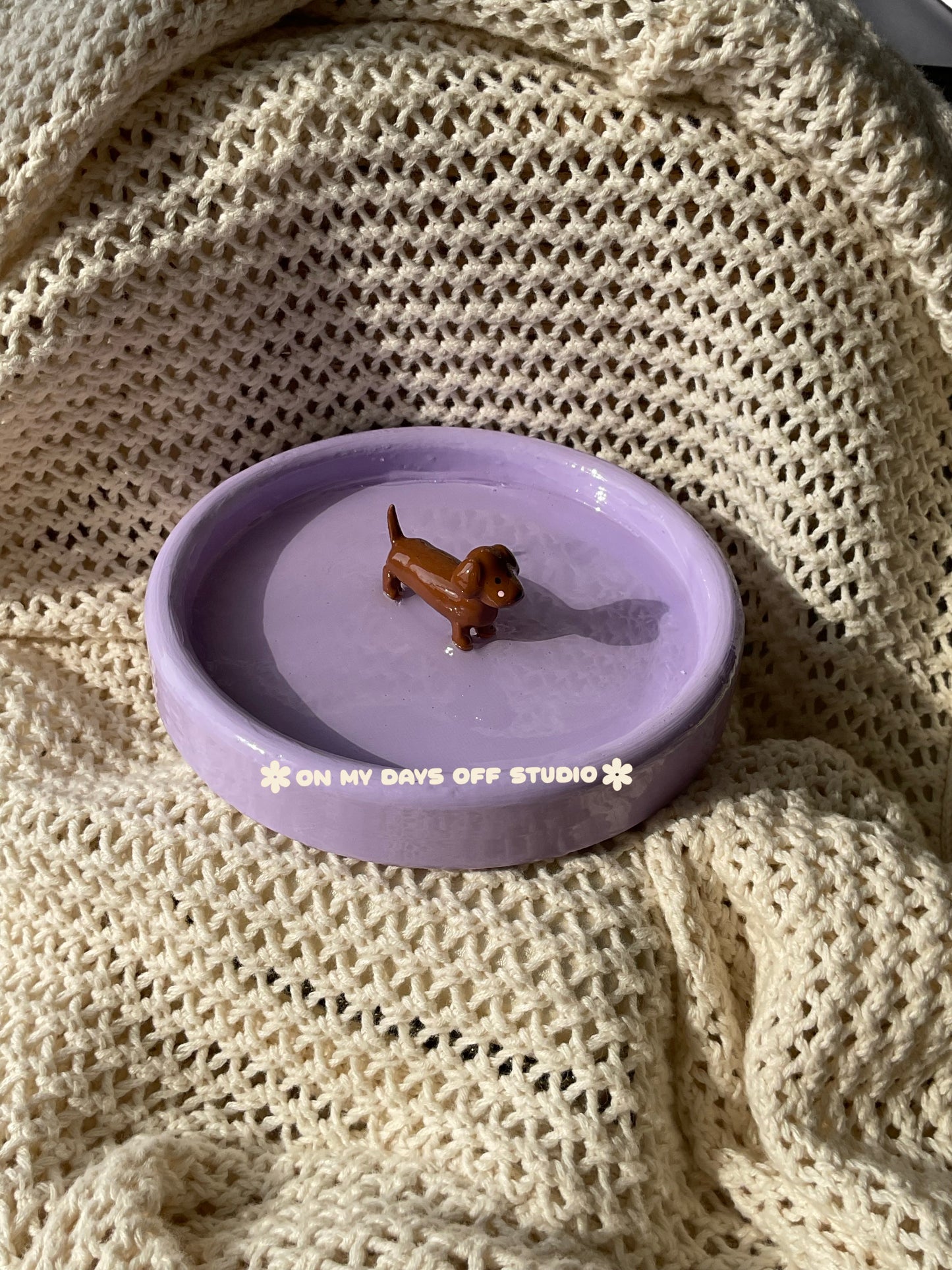 Small brown dachshund figurine on a purple jewelry dish or trinket dish