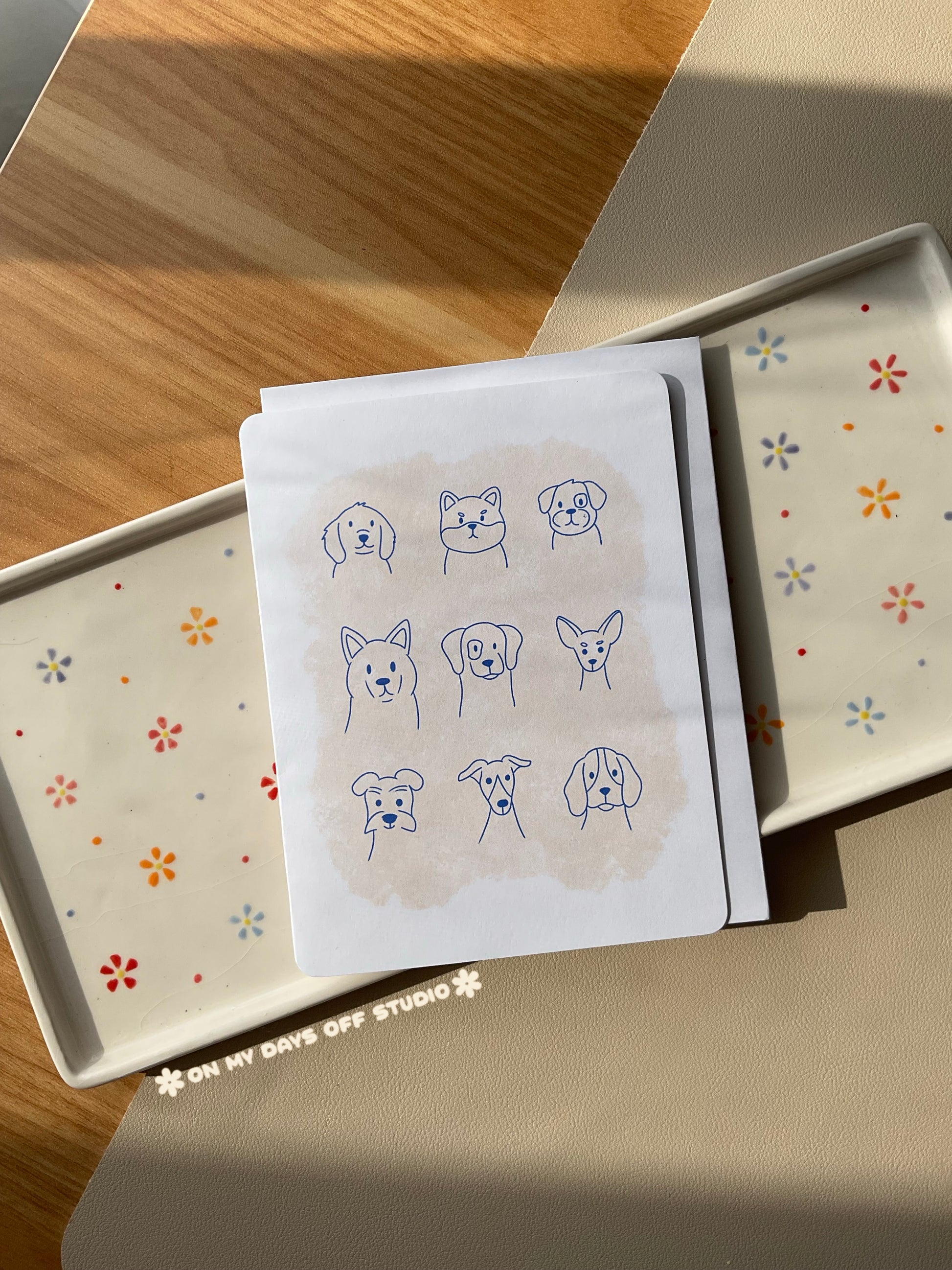 White greeting card with a cute line drawings of 9 dogs with a abstract beige background. Blank interior for your personal handwritten message. 