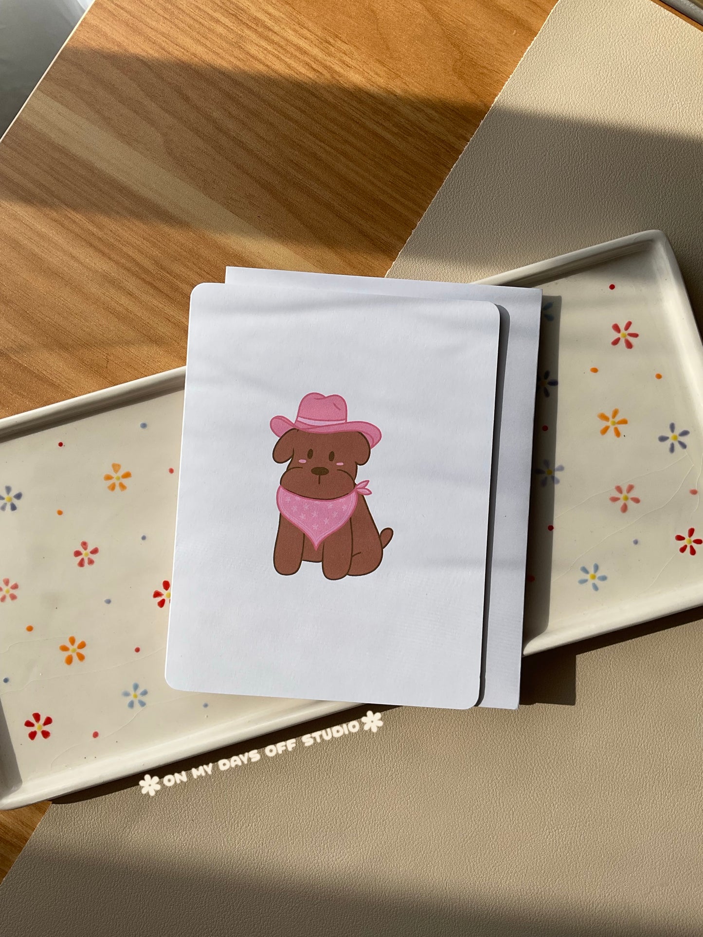 White greeting card with a cute illustration of a puppy in a pink cowgirl hat and triangle scarf. Blank interior for your personal handwritten message. 